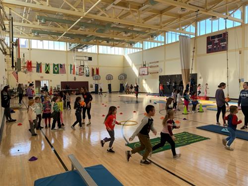 Many students in the Mullen-Hall gymnasium rotating around stations during their fitness day 